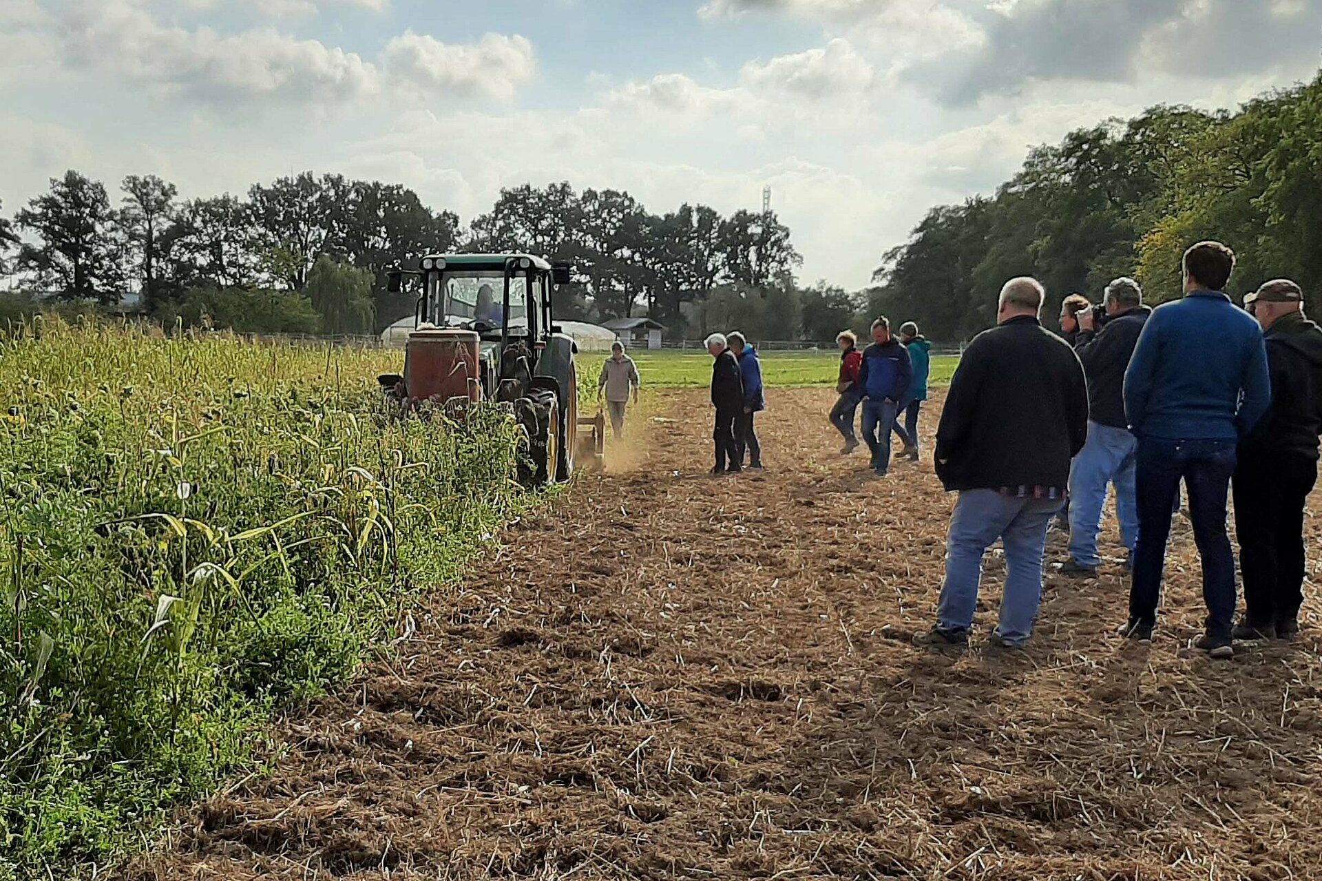 Traktor beim Mulchen, daneben eine Gruppe Menschen.